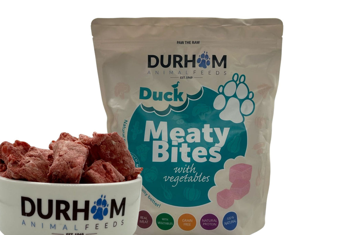 Durham Duck Meaty Bites with vegetables in a turquoise-labelled bag beside a bowl of frozen bites.